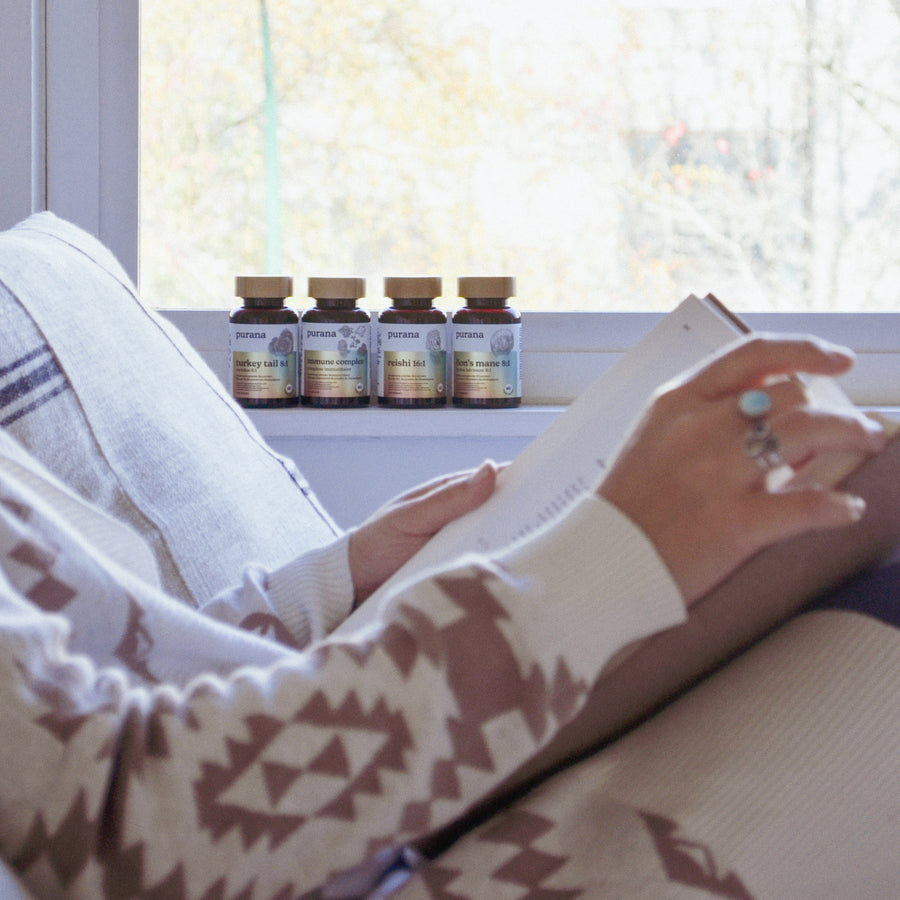 Four Purana bottles on a bright window sill with a hand reaching for one
